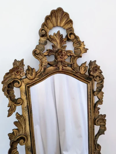 Miroir ancien vertical avec cadre en bois et stuc doré richement sculpté de motifs rocaille, volutes et fronton