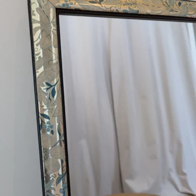 Grand miroir vintage rectangulaire à motif feuillage vert sur fond doré avec cadre noir fin, style nature chic.