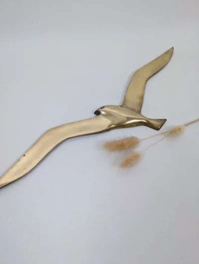 Statuette vintage d'oiseau en laiton doré avec détails ciselés sur les ailes et la queue, posée sur une surface blanche.