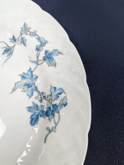 Détail d'une assiette en porcelaine de Limoges Bernardaud modèle Saint-Saëns avec décor de feuilles de vigne bleues et bordure en relief tressé.