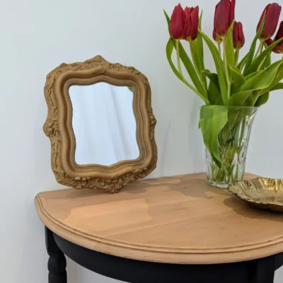 Petit miroir ancien en plâtre doré posé sur une console avec des tulipes rouges