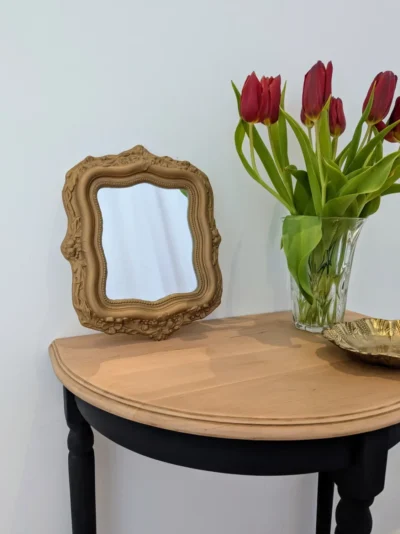 Petit miroir ancien en plâtre doré posé sur une console avec des tulipes rouges