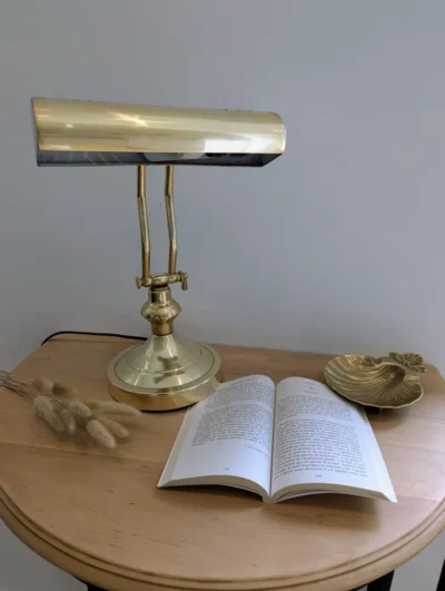 Lampe de notaire ancienne en laiton doré poli style piano sur un bureau en bois avec un livre ouvert et un vide-poche coquille.