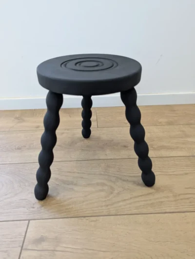 Petit tabouret tripode vintage revisité en bois peint noir mat, assise ronde et pieds biseautés, style néo-rustique.