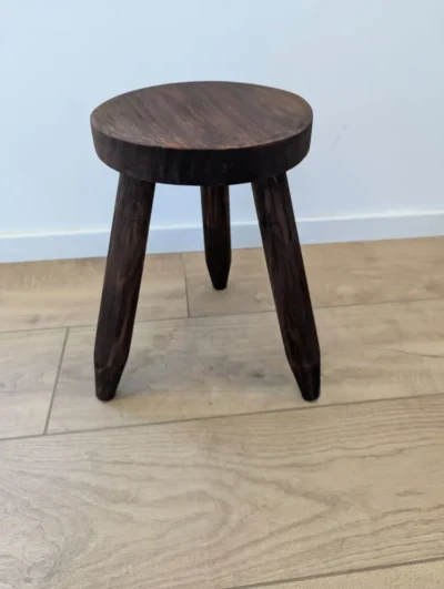 Petit tabouret tripode ancien en bois clair avec trois pieds fuselés et assise circulaire, style mobilier de ferme.