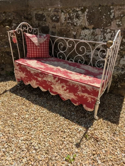 Lit banquette ancien en fer forgé blanc cassé avec matelas en toile de Jouy rouge et pommeaux en laiton.