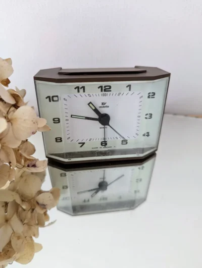 Réveil Vedette quartz vintage des années 70, boîtier moderniste noir mat et cadran blanc à chiffres arabes, horlogerie française de précision.