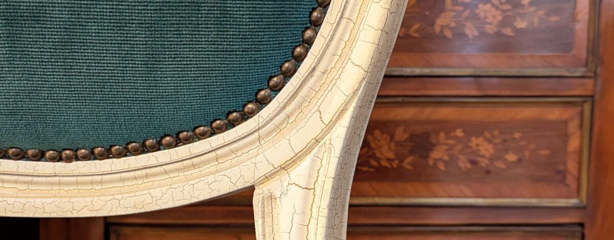 Siège ancien restauré Villa Brieg : détail de patine sur bois laqué, tapisserie verte et meuble en marqueterie pour un intérieur vintage de caractère.