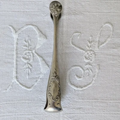 pince à sucre Christofle modèle Rocaille en métal argenté, décor Louis XV sur linge brodé, Villa Brieg