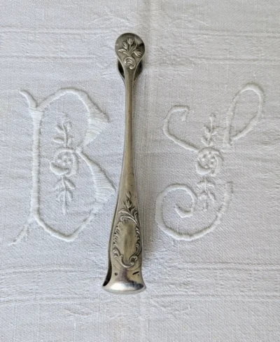 pince à sucre Christofle modèle Rocaille en métal argenté, décor Louis XV sur linge brodé, Villa Brieg