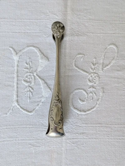 pince à sucre Christofle modèle Rocaille en métal argenté, décor Louis XV sur linge brodé, Villa Brieg