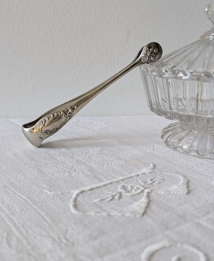 pince à sucre Christofle modèle Rocaille en métal argenté, décor Louis XV sur linge brodé, Villa Brieg