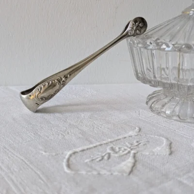 pince à sucre Christofle modèle Rocaille en métal argenté, décor Louis XV sur linge brodé, Villa Brieg