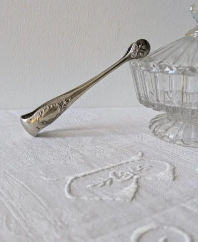 pince à sucre Christofle modèle Rocaille en métal argenté, décor Louis XV sur linge brodé, Villa Brieg