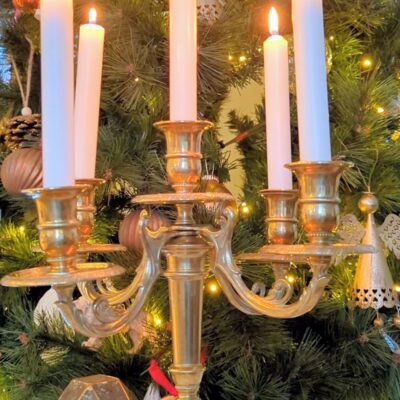 Chandelier ancien en laiton avec bougies allumées devant décor de Noël