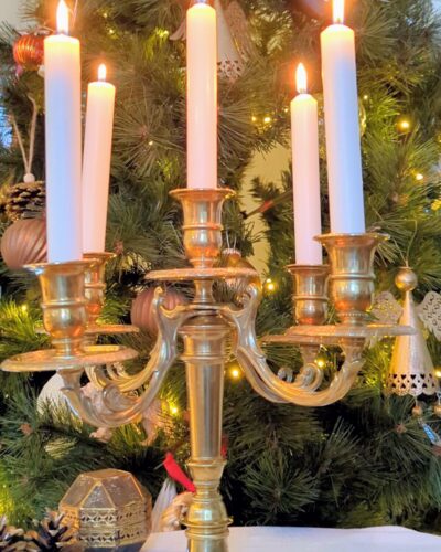 Chandelier ancien en laiton avec bougies allumées devant décor de Noël