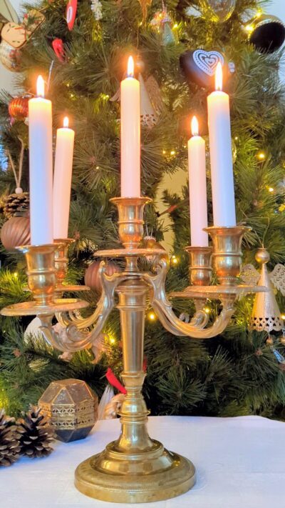 Chandelier ancien en laiton avec bougies allumées devant décor de Noël