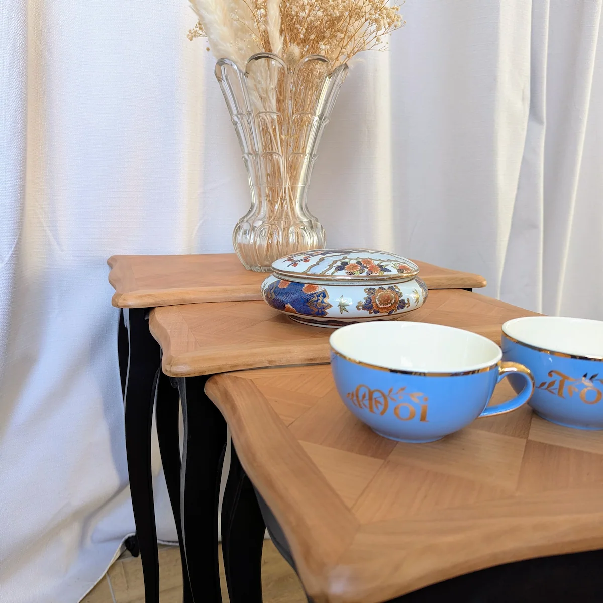 Table gigogne ancienne avec tasses bleues et vase de fleurs séchées