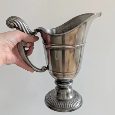 Main tenant une aiguière en étain pour échelle