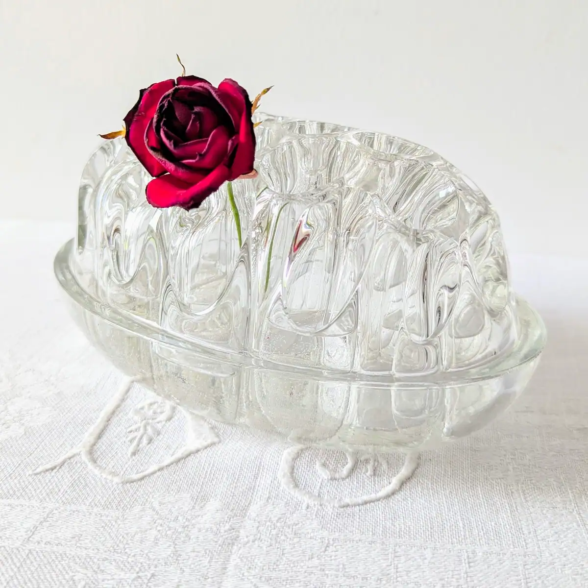 Rose rouge unique maintenue dans un pique-fleurs vintage en verre