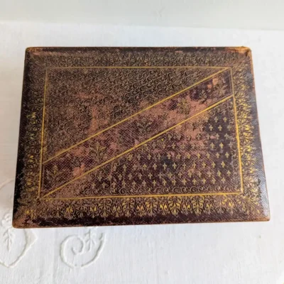 Détail du dessus d'une boîte à bijoux en cuir ancienne avec motifs fleurs de lys.