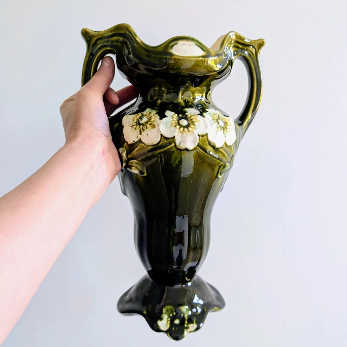 Grand vase ancien en barbotine verte tenu à la main pour l'échelle