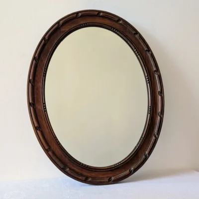 Miroir ancien ovale en bois sculpté brun de face sur mur blanc