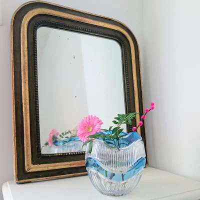 Vase bleu en cristal posé devant un miroir ancien à cadre doré