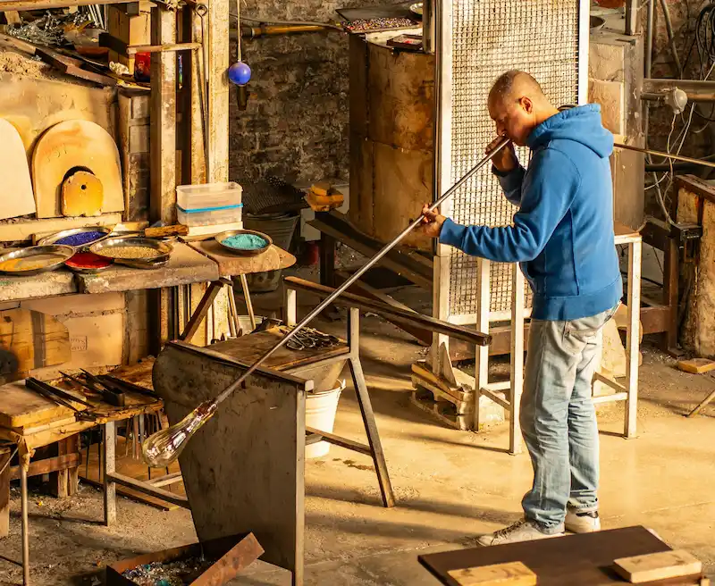 Artisan souffleur de verre utilisant une canne dans un atelier traditionnel