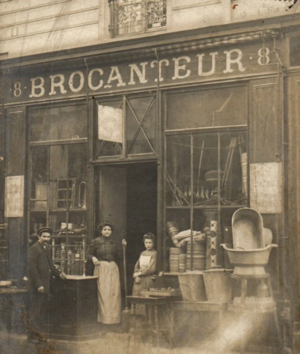 Photographie d'époque de la façade d'un brocanteur parisien à la Belle Époque, illustrant le commerce d'antiquités traditionnel.