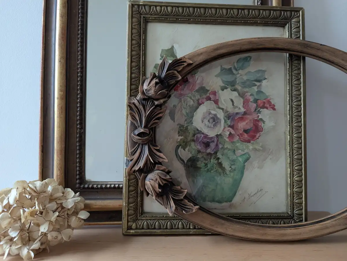 Cadre ovale ancien en bois sculpté patiné posé devant une peinture rétro de fleurs