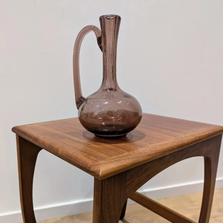 Carafe Biot en verre bullé prune posée sur une table d'appoint vintage en bois.