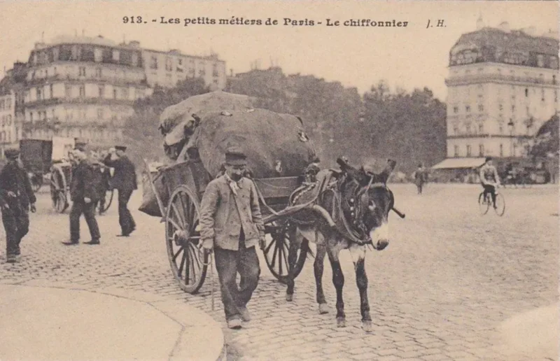 Carte postale ancienne des petits métiers de Paris montrant un chiffonnier et son attelage tracté par un âne sur une place pavée.