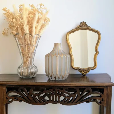 Décoration ancienne en ligne mettant en scène un vase art déco doré et un miroir vintage sur une console en bois foncé