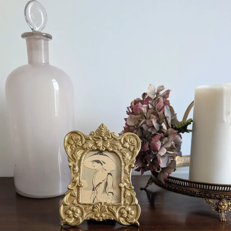 Cadre ancien doré et flacon en verre opalin sur un meuble en bois sombre pour une décoration vintage de luxe.