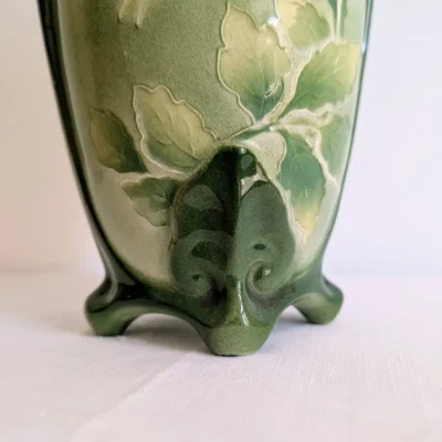 Gros plan sur les pieds nervurés et les motifs de roses en relief du vase ancien