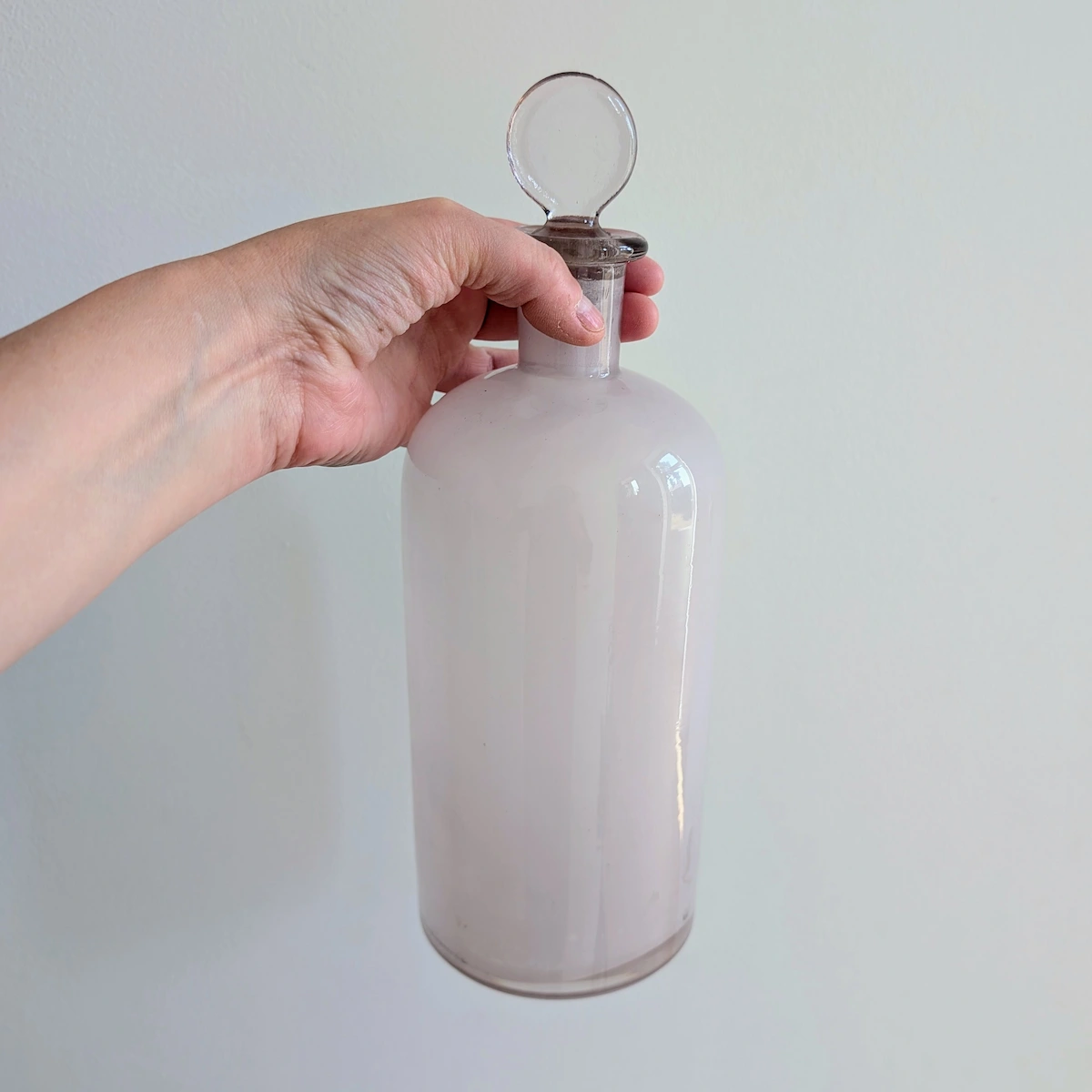 Le flacon d'apothicaire ancien est tenu à pleine main par le corps du verre pour montrer sa grande taille.