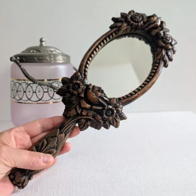 Miroir ancien en bois sculpté tenu en main pour échelle