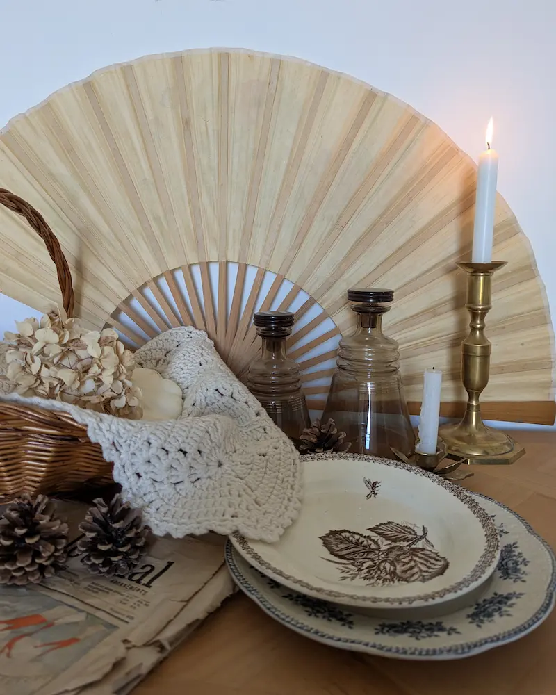 Table dressée avec vaisselle ancienne en terre de fer, éventail en bambou et bougie pour une ambiance nostalgique.