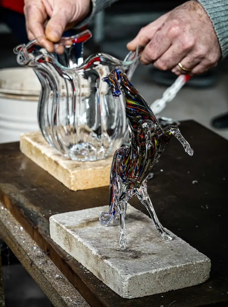 Sculpture de cheval en verre multicolore et vase en verre ondulé sur un plan de travail d'atelier