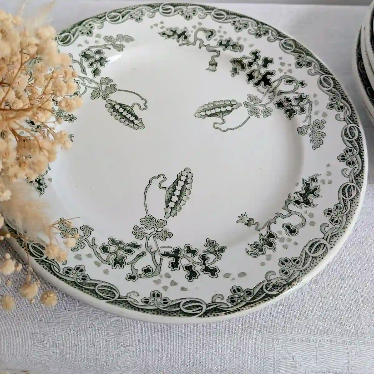 Assiette en faïence verte Saint-Amand disposée sur une table esprit campagne chic à côté de fleurs séchées.