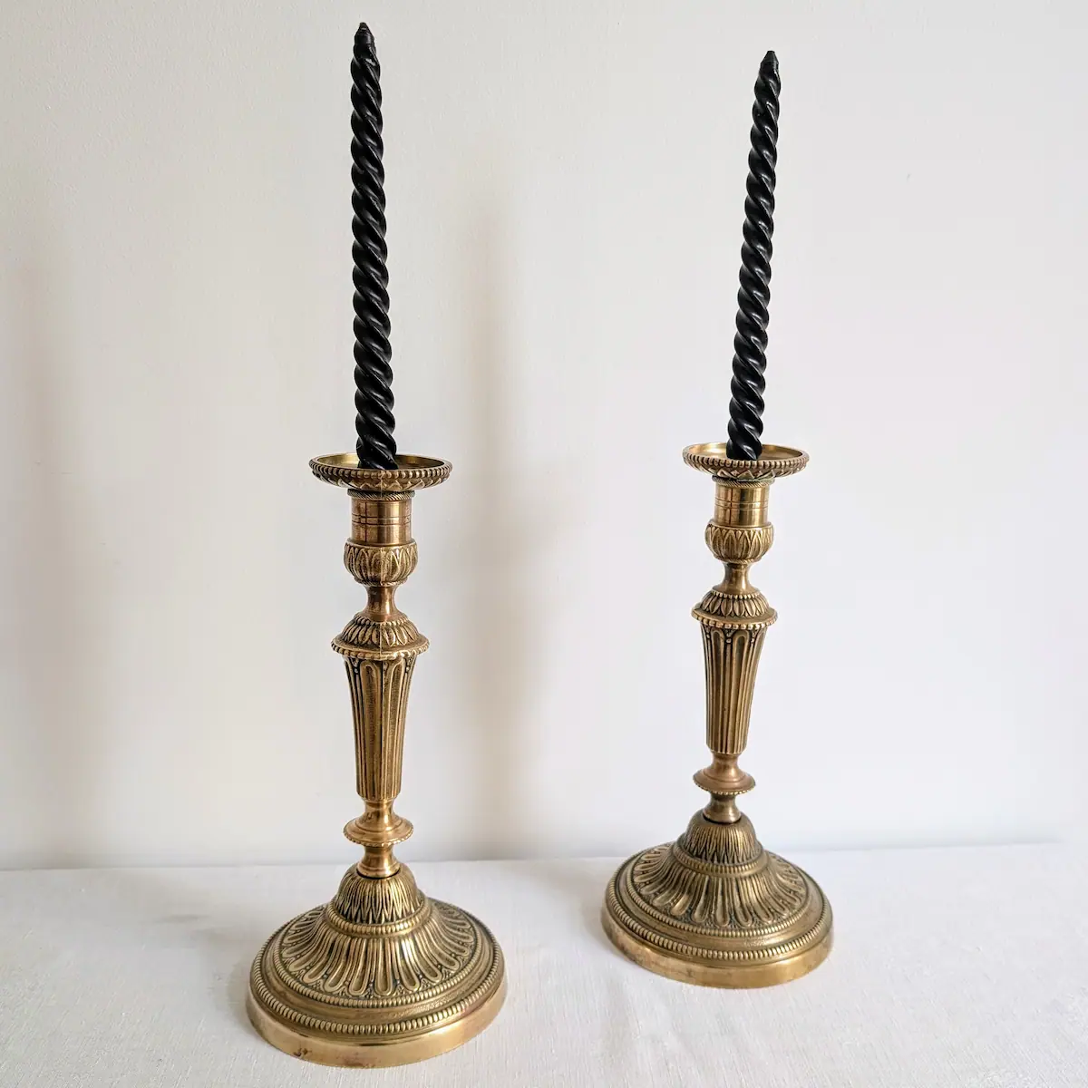 Paire de bougeoirs anciens en laiton ornés de longues bougies torsadées noires.