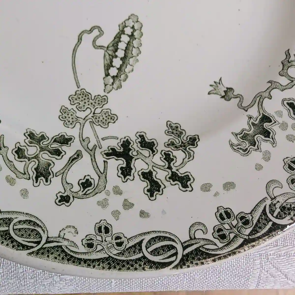 Gros plan sur le décor imprimé vert de muguet et de feuillages stylisés Art Nouveau sur le marli.