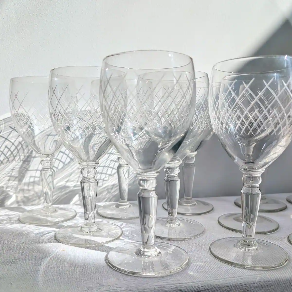 Verres à vin en cristalin gravé projetant des ombres de croisillons sur la table