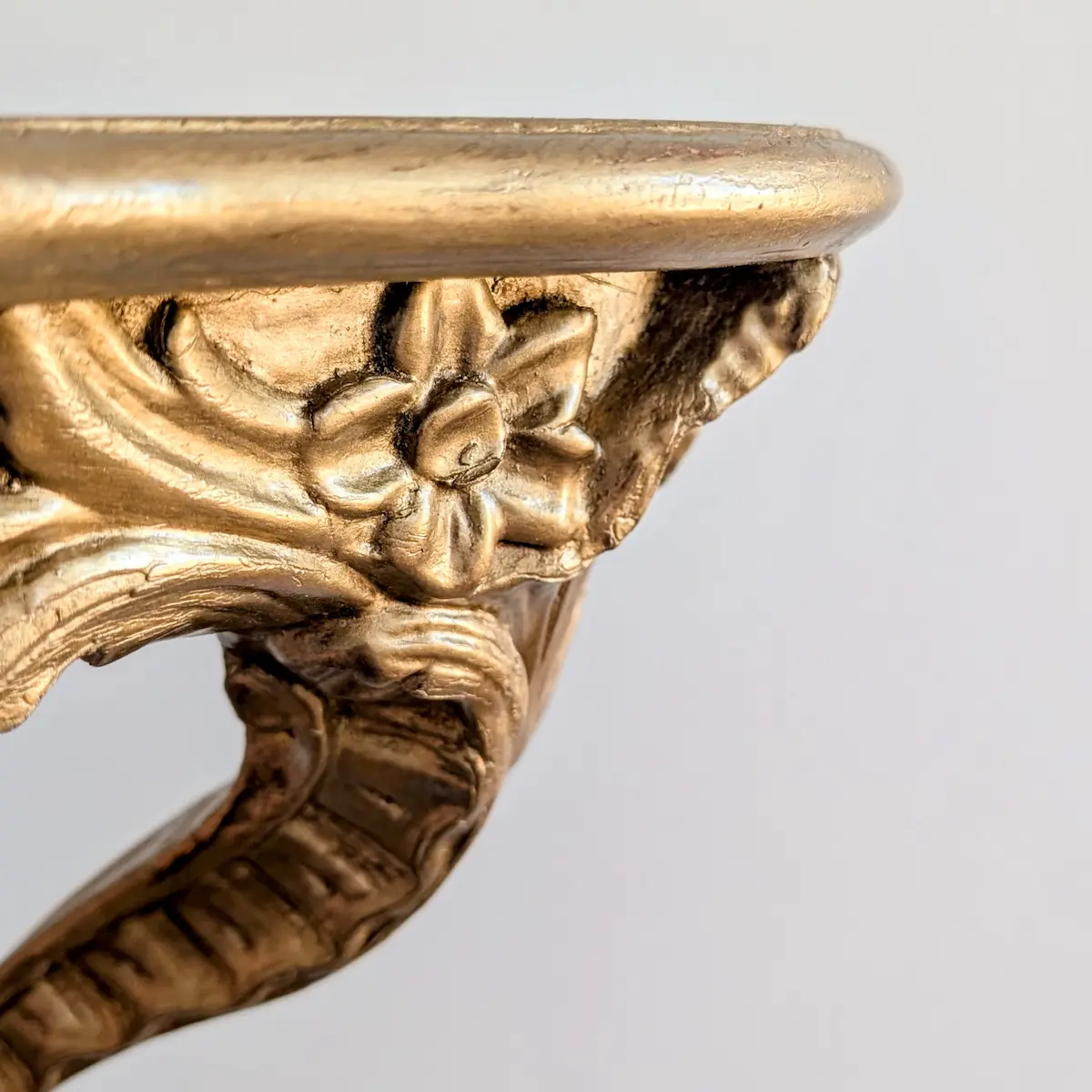 Gros plan sur la sculpture florale et la patine dorée d'une console ancienne