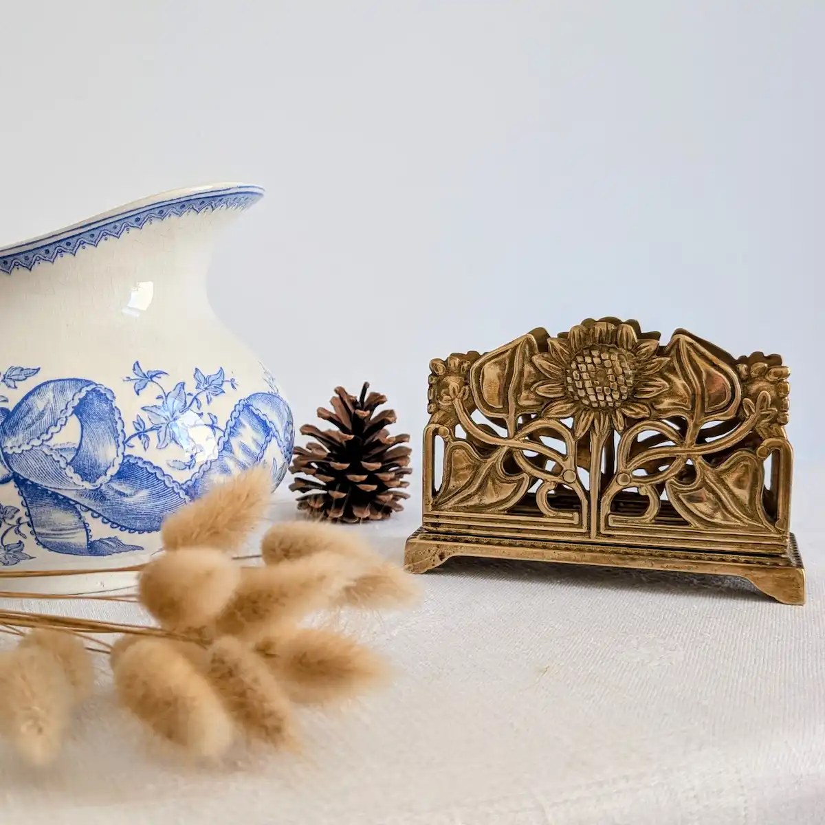 Porte-courrier en laiton posé sur une table aux côtés d'une cruche ancienne et de fleurs séchées