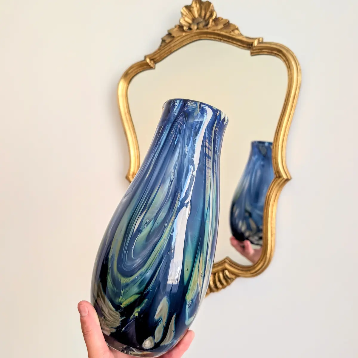 Vase décoratif en verre soufflé présenté devant un miroir doré