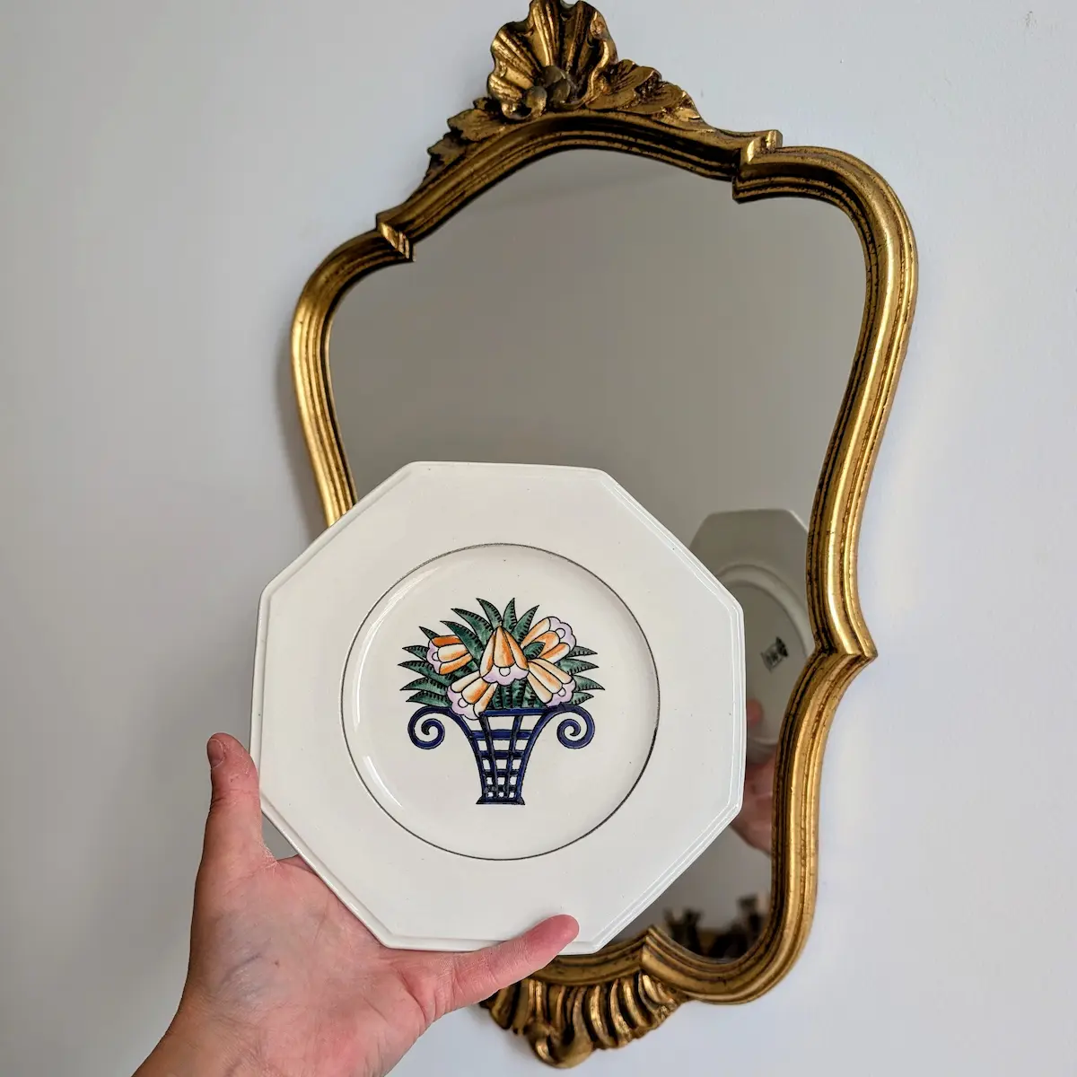 Assiette dessert Longwy faïence tenue en main devant un miroir doré d'époque