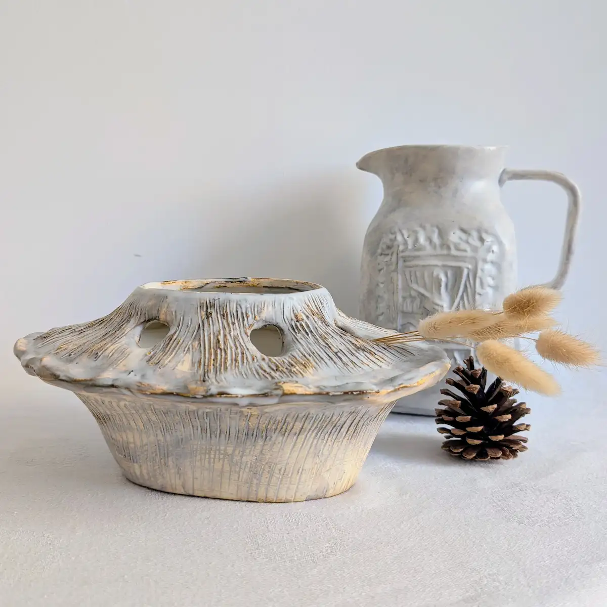 Bouquetière vintage posée sur une table aux côtés d'un pichet en céramique