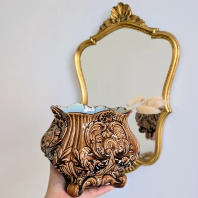 Cache-pot ancien en barbotine tenu en main devant un miroir doré d'époque.